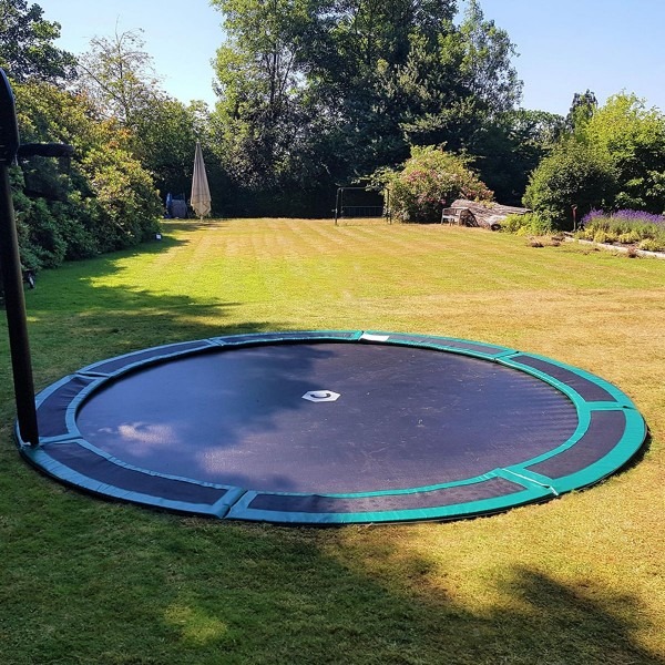 An in ground trampoline under a shaded area in a backyard.